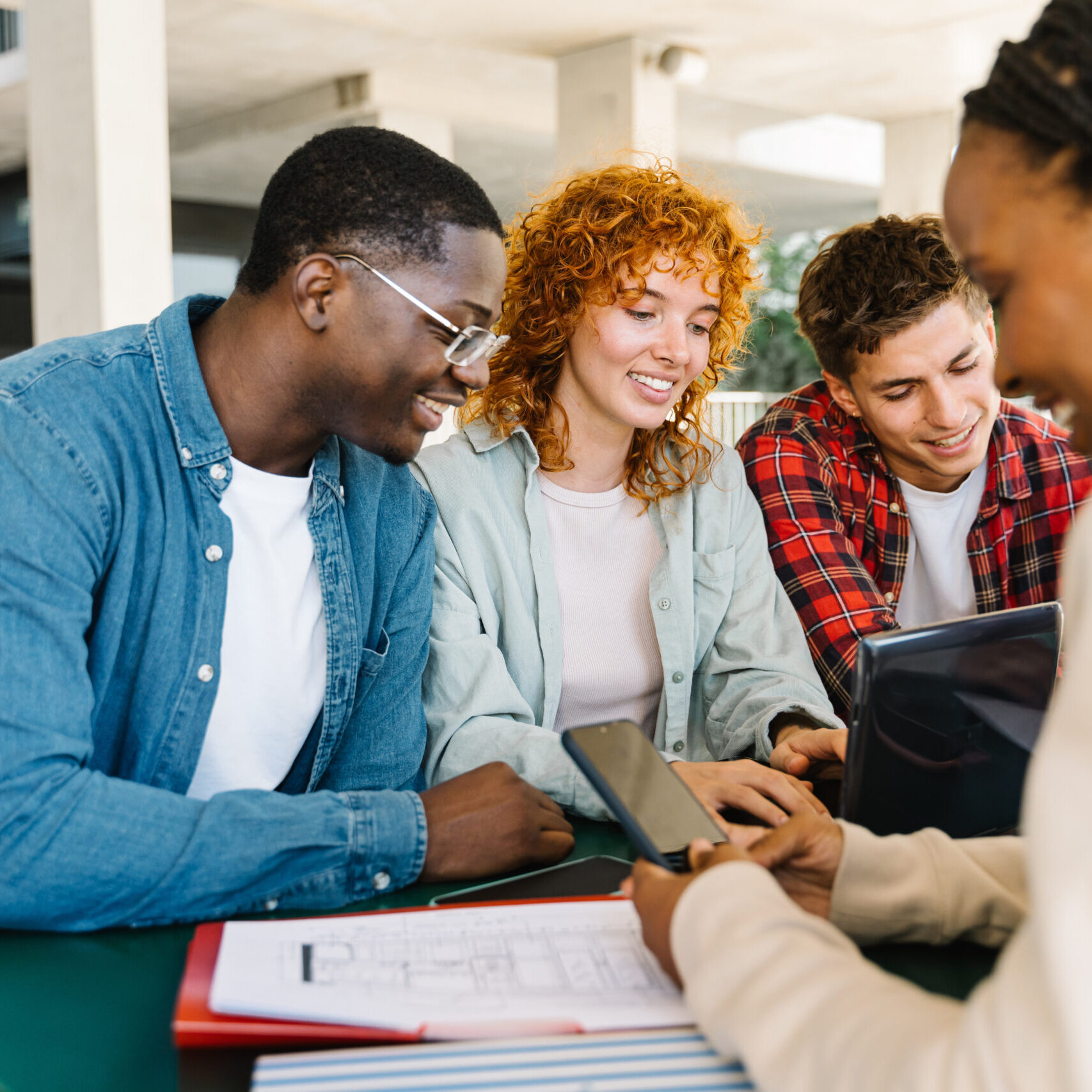 University students sitting around a table studying together happy and typing on the laptop and mobile phone